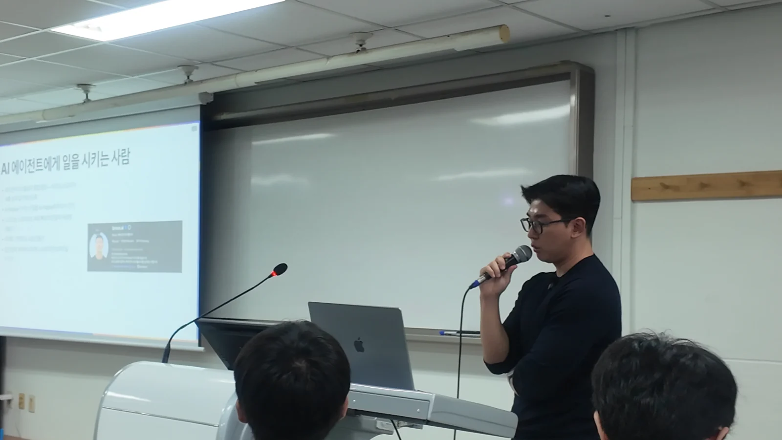 강의실 — AWC 강사가 「AI 에이전트에게 일을 시키는 사람」 슬라이드 옆에서 설명하는 모습